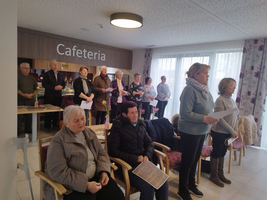 Eine Gruppe von Menschen steht in einer Cafeteria und hält Unterlagen in der Hand.