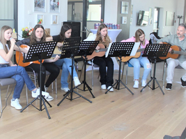 Sechs Personen spielen Gitarre und singen in einem geräumigen Raum.