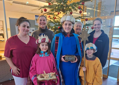 Kinder und Erwachsene verkleidet als Heilige Drei Könige vor einem Weihnachtsbaum.