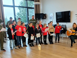 Kinder singen gemeinsam, während eine Frau Gitarre spielt.