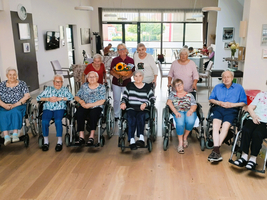 Gruppe älterer Menschen in Rollstühlen, lächelnd in einem Gemeinschaftsraum.
