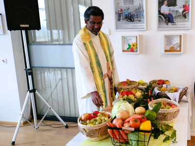 Ein Priester steht neben einem Tisch mit verschiedenen Obst- und Gemüsekörben.