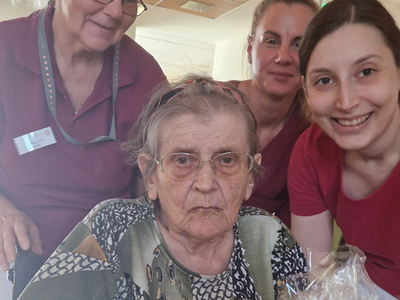 Eine ältere Frau mit Geschenken umgeben von drei Pflegekräften.