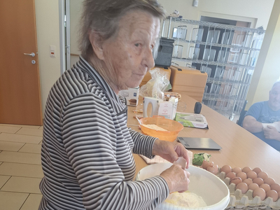 Eine ältere Frau bereitet Teig in einer Schüssel auf einer Küchentheke vor.