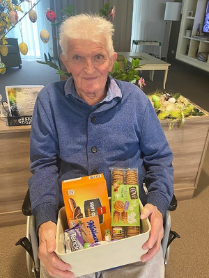 Ein älterer Mann mit einem Behälter voller Snacks sitzt im Rollstuhl.