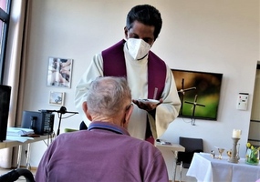 Ein Priester reicht einer älteren Person in Pflege eine Oblate.