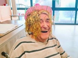 Älterer Mann mit lustigem Hut und glitzerndem Haar, lächelt fröhlich.