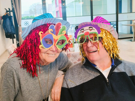 Zwei ältere Personen tragen bunte Gesichtsmasken und lustige Perücken beim Feiern.