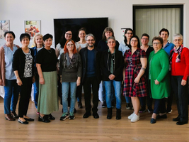 Gruppe von 15 Personen in einem Raum, lächelnd und posierend für ein Foto.