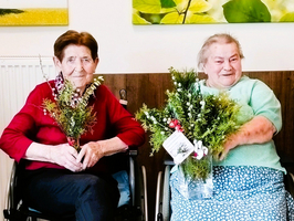 Eine Gruppe älterer Frauen in Rollstühlen hält Blumensträuße.