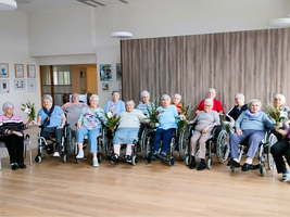 Eine Gruppe älterer Frauen in Rollstühlen hält Blumensträuße.
