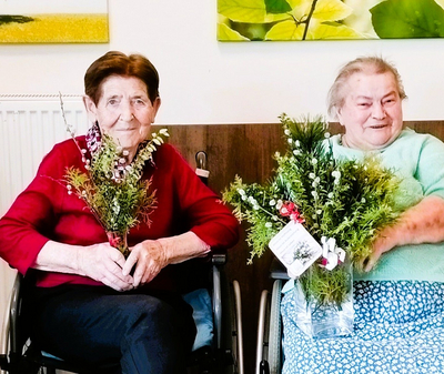 Eine Gruppe älterer Frauen in Rollstühlen hält Blumensträuße.