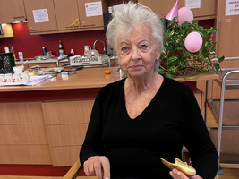 Eine ältere Frau sitzt am Tisch und isst ein Frühstück mit Brötchen und Rührei.