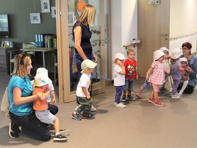 Kinder mit Erzieherinnen in einem Flur, einige halten einen Seil.