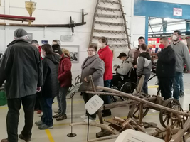 Besuchergruppe in einem Museum, umgeben von alten landwirtschaftlichen Geräten.