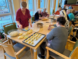 Ältere Menschen backen gemeinsam an einem Tisch in einem Gemeinschaftsraum.