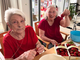 Zwei ältere Frauen schälen Erdbeeren in einem hellen Raum.