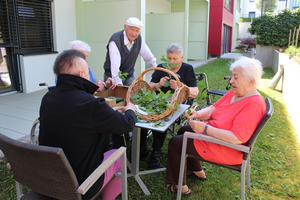 Ältere Menschen sitzen gemeinsam und sortieren frische Kräuter im Freien.