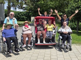 Gruppe älterer Menschen und Betreuer genießt den Sonnenschein im Freien.