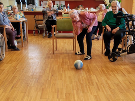 Ältere Menschen spielen mit einer Kugel Bowling in einem Gemeinschaftsraum.