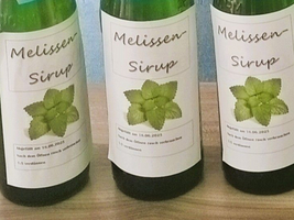 Flaschen mit Melissensirup und einem grünen Blattmuster auf dem Etikett.