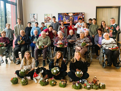 Gruppenfoto mit Senioren und Kindern, die weihnachtliche Dekorationen halten.