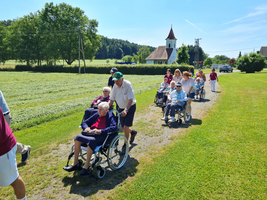 Eine Gruppe von Senioren im Rollstuhl wird von Betreuern im Freien begleitet.