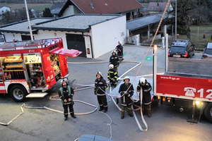 Feuerwehrleute stehen neben einem Löschfahrzeug und bereitliegenden Schläuchen.