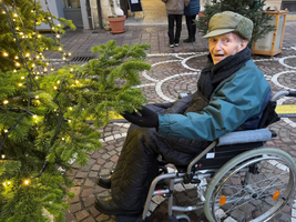 Älterer Mann im Rollstuhl interagiert mit einem geschmückten Weihnachtsbaum.