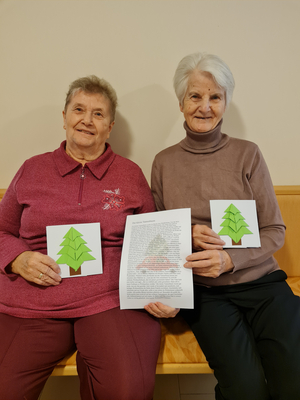 Zwei ältere Frauen halten Tannenbaum-Karten und ein Dokument mit Text.