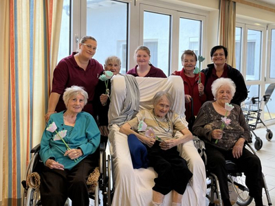 Gruppenfoto von Senioren in Rollstühlen mit Blumen in einer Einrichtung.
