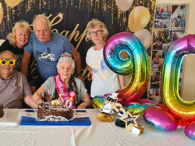 Ein älteres Paar feiert den 90. Geburtstag mit Kuchen und Gratulanten.