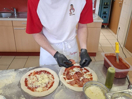 Ein Mann belegt zwei Pizzaböden mit Tomatensoße, Käse und Salami.