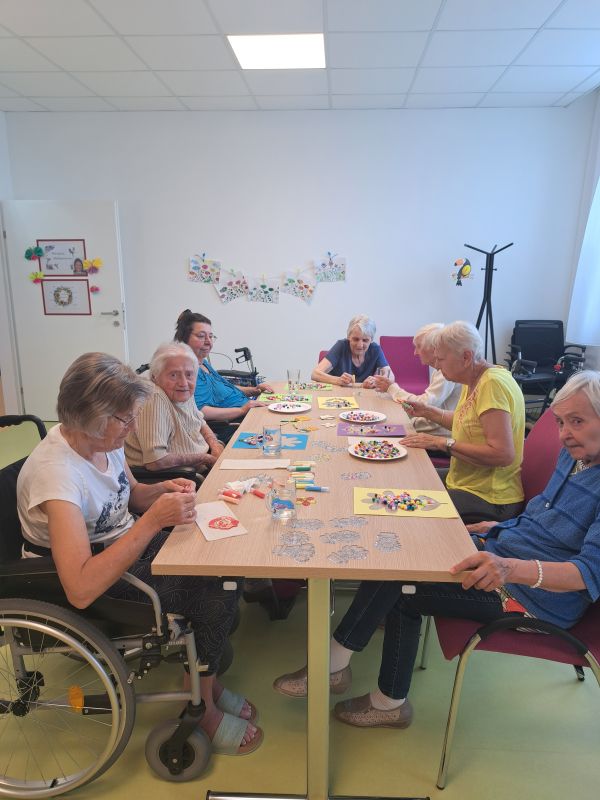 Ältere Frauen arbeiten gemeinsam an Bastelprojekten an einem Tisch.