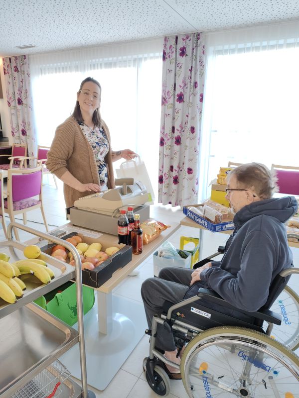 Eine Frau steht an einer Kasse, ein Mann im Rollstuhl kauft ein.